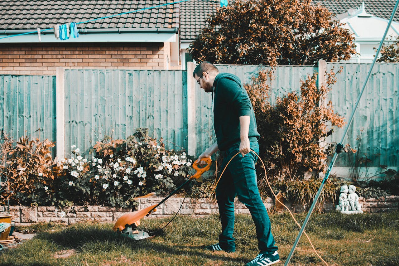 about-us A man using an electric mower in a garden on a sunny day, capturing outdoor chores and gardening vibes.